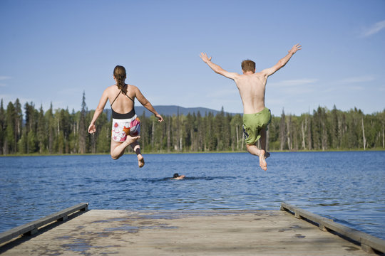 Young man and woman jumping off the end of a lake pier