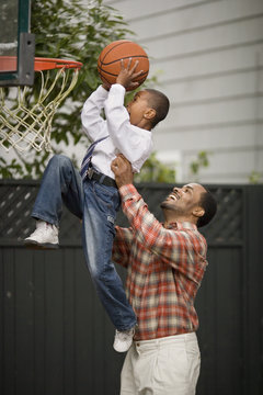 Father lifting his son up to a basketball hoop.