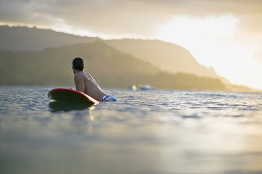 Male surfer balances on his surfboard in a calm sea with coastline in the background.