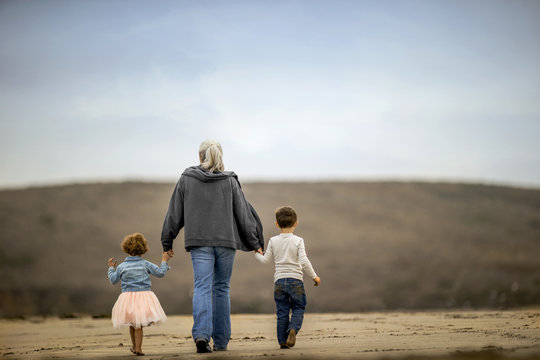 Mature woman walking on the beach with her grandchildren.