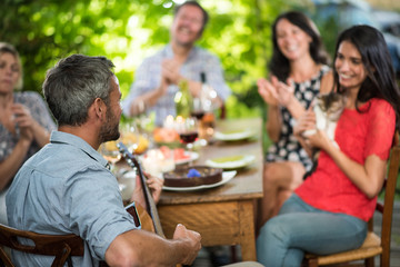 Summertime, man playing guitar for his friends on a terrace