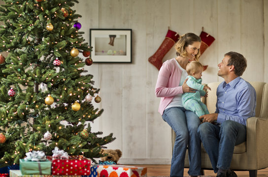 Couple and their baby sitting next to the Christmas tree.