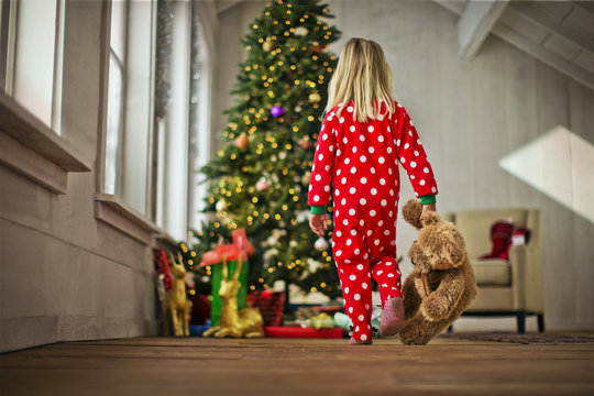 Young girl walking towards the Christmas tree with her teddy bear.