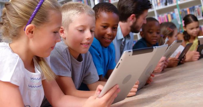 School kids and teacher using digital tablet in library at school 4k