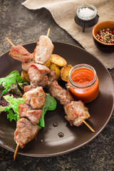 Shish kebab with greens, potatoes and sauce on ceramic plate