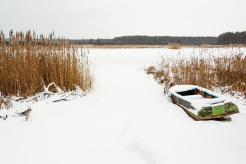 Old boat at the shore of a frozen river with reeds