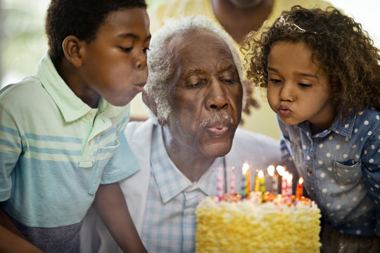 Senior man blowing out his birthday candles with his family