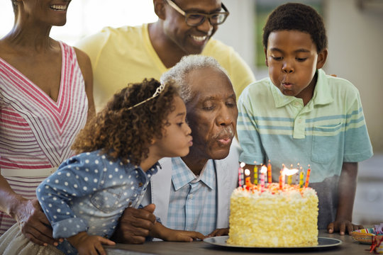 Senior man blowing out his birthday candles with his family.