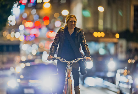 Smiling young woman riding her bicycle along a busy city road at night.