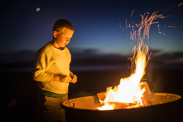 Boy looking at glowing campfire at the beach