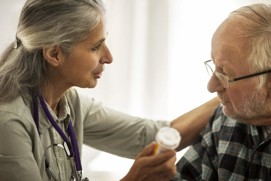 Female doctor speaking with an elderly male patient while holding a bottle of medication.