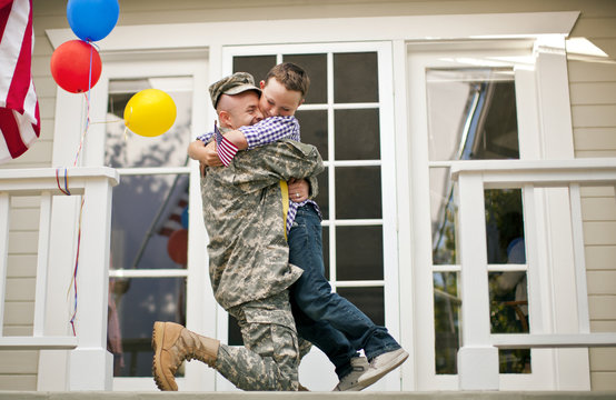 Happy army soldier hugging his young son on the porch of their home.