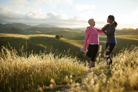 Young woman helping a senior woman to stretch while exercising in a rural landscape.