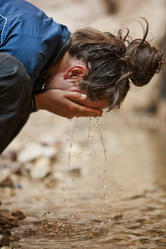 Young woman splashing water from a stream onto her face.