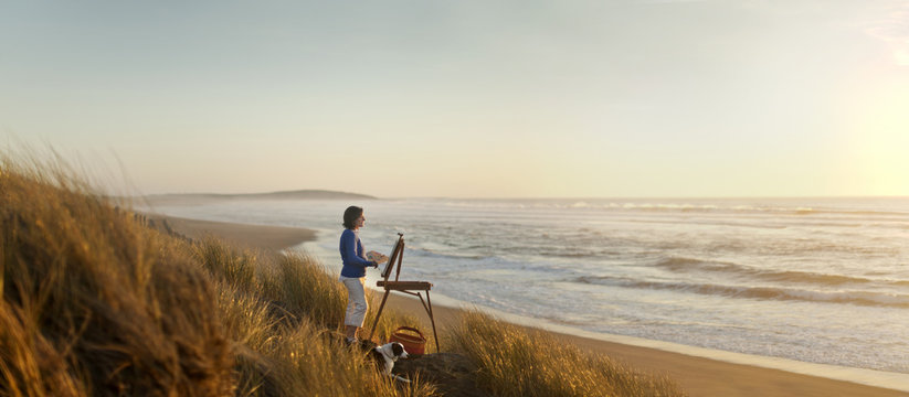 Content mature woman painting a beach scene at sunset.