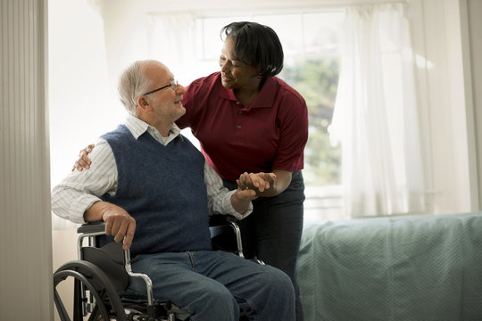 Smiling female nurse comforting an elderly male patient in a wheelchair.
