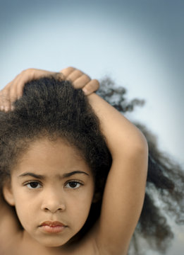 Portrait of a young girl with curly black hair standing with her arms above her head.