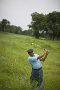 Senior man swinging a golf club in tall green grass