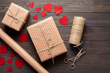 Fototapeta na wymiar Flat lay composition with gifts, scissors, wrapping paper, twine, woolen hearts. Packaging of gifts in rustic style on Valentine's Day, a birthday, Mother's Day or Christmas. Dark wooden background.