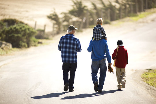 Grandfather walking with his son and grandsons along a country road.