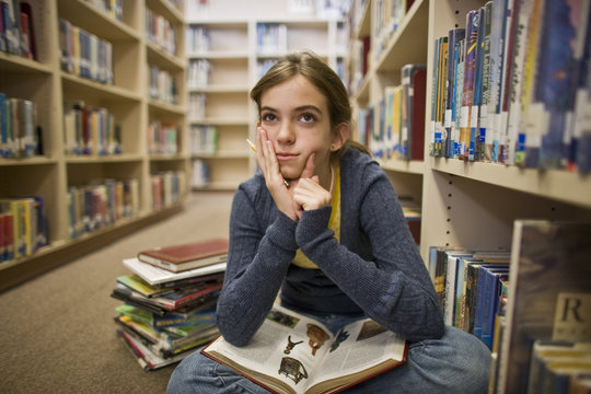 Thoughtful teenage girl reading books in a library.