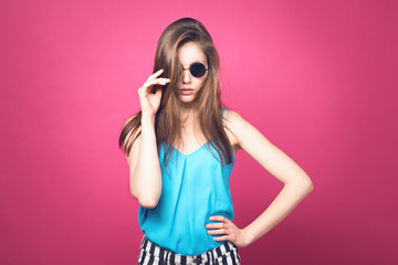 Beautiful fashionable woman in black sunglasses. Pink background. Girl in sunglasses. Round glasses. Toned image.