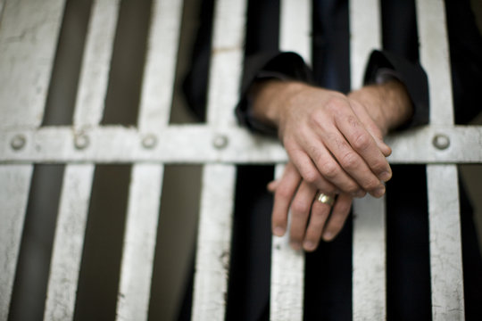 Hands of a mature businessman through bars of a cell in a derelict building.