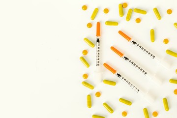 insulin syringe, pills and capsules on half of white background.