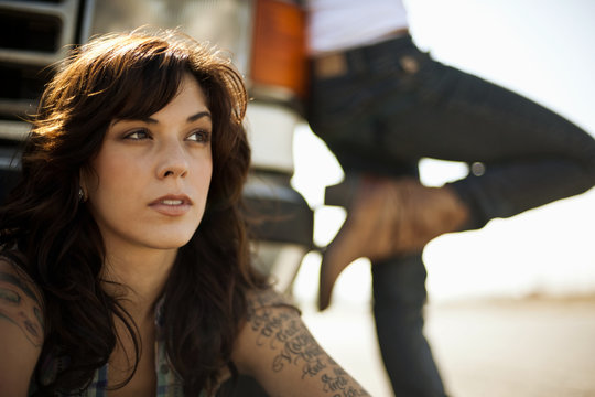 Two female friends leaning against their broken down car.