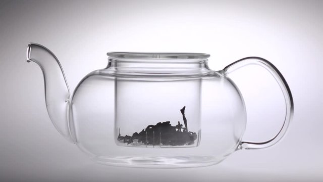 Two tablespoons of tea poured in transparent teapot. White background