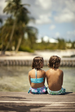 Two happy young children relaxing on a wooden pier on their tropical island holiday.