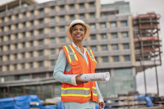 Proud young female engineer holding a roll of building plans on a construction site.