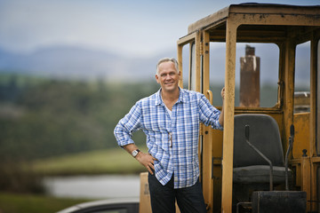 Portrait of a middle aged farmer standing by a mechanical digger.