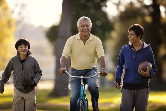 Smiling senior man having fun riding a bicycle while in a park with his two grandsons.
