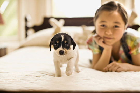 Little girl rests on her chin on her hand as she lies on a bed with a puppy to pose for a portrait.