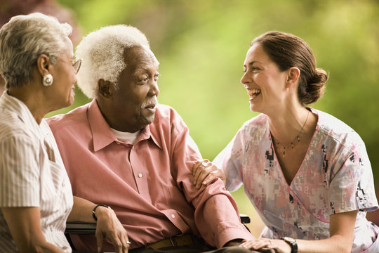 Senior couple talk with a smiling nurse as they sit together outside.