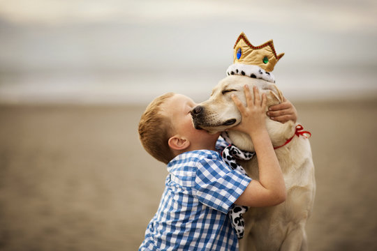 Boy kissing his dog while sitting on beach