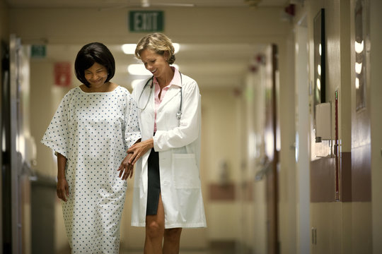 Doctor helping patient to walk through the corridor after surgery