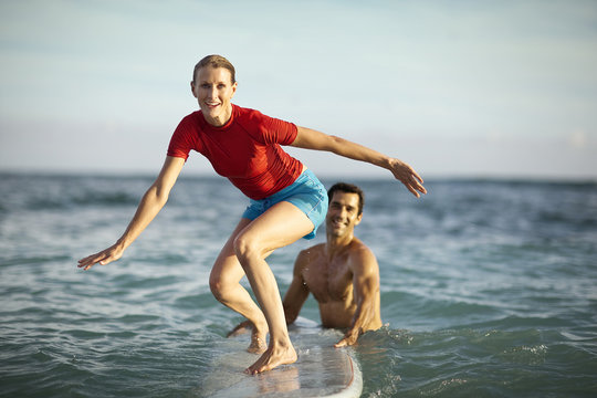 Mid-adult woman learning how to surf with the help of her boyfriend.