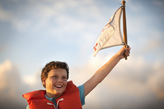 Young boy wearing a life jacket waves a flag.