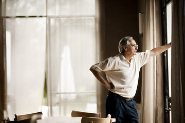Senior man looking through window while standing at home