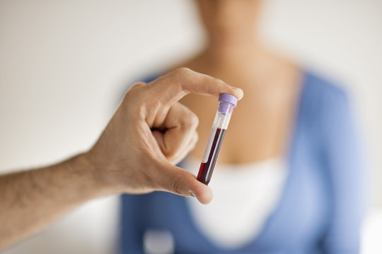 Male hand holding vile of blood between his fingers.