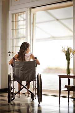 Young girl in a wheelchair at home,  looking outside.