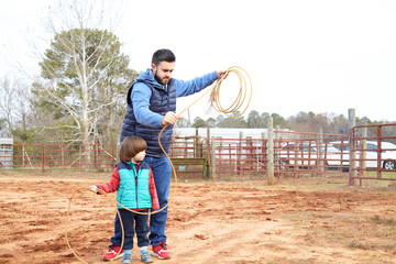 Father training small toddler boy son making loope and throwing lasso to bull in the ranch. Roping...