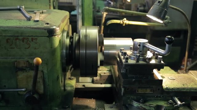At the factory old horizontal lathe aligns layer of metal parts. Mechanism moves perfectly smoothly and aligns the cylinder surface from which steam coming from the heat caused by friction. Over a