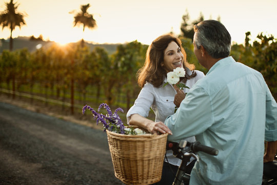 Happy mature couple putting flowers in basket of their bicycle.