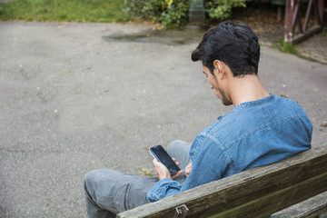 Obraz premium Trendy handsome young man using cell phone sitting on bench