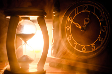 Time concept. Silhouette of Hourglass clock and old vintage wood clock with arrow and smoke on dark...