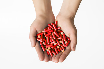 Hands is giving red capsules and orange pills on white background.