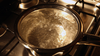 Shining bubbles of boiling water in a stainless stewpan on a gas oven
